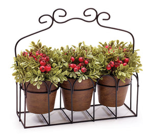 Three artificial green plants with red berries displayed in a decorative metal caddy
